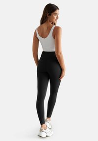 Schwarze hochtaillierte Leggings, kombiniert mit einem weißen Tanktop, das eine glatte Textur und eine figurschmeichelnde Passform aufweist, getragen mit weißen Sportschuhen.