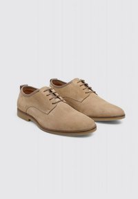 Zapatos de vestir de ante beige con un acabado suave, punta redonda y diseño clásico de cordones. Suela marrón claro, con detalles de costura sutil.