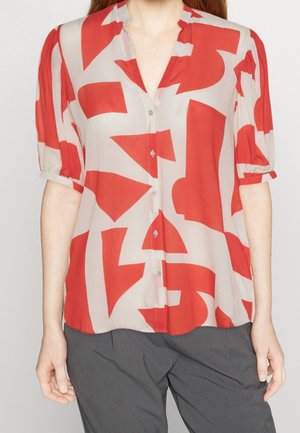 Blusa rossa e beige con motivo astratto, tessuto morbido, chiusura con bottoni frontale e maniche corte a sbuffo. Leggera texture nel materiale.