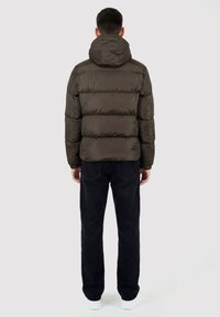 Giacca a piumino verde oliva con cappuccio, caratterizzata da un design trapuntato e una texture leggermente lucida. Abbinata a jeans neri a gamba dritta.