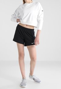Sudadera blanca corta con cuello redondo, pantalones cortos negros y zapatos deportivos grises. Logo de Nike en la manga de la camiseta y en los pantalones cortos. Textura suave.