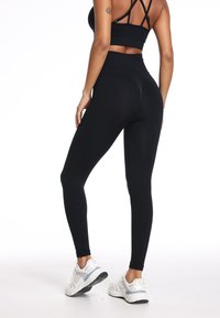 Zwarte legging met een hoge taille, een gladde textuur en een aansluitende silhouette. Gecombineerd met witte sportieve schoenen voor contrast.