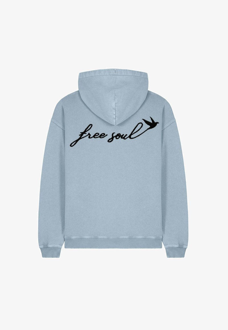 Haut de survêtement bleu clair avec capuche à cordon. Présente un texte en cursive noir "free soul" et un petit dessin d'oiseau à l'arrière. Texture douce.