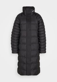 Svart vadderad kappa med hög krage och tryckknappar. Har quiltat mönster och ribbade detaljer fram och på ärmarna. Tillverkad av ett jämnt material.