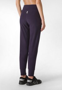 Marineblauwe katoenen joggers met aansluitende boorden en een hoge tailleband, met een klein label op de achterkant. Gemaakt in combinatie met zwarte sportschoenen.