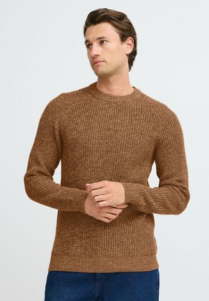 Maglione marrone a maglia con superficie texturizzata, scollo rotondo e maniche lunghe, abbinato a pantaloni in denim blu.