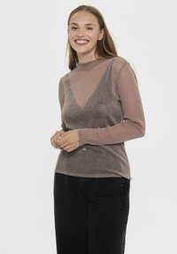 Garums piedurkņu tops no viegla, spīdīga mauve auduma ar augsto apkakli un pielāgotu siluetu, kombinēts ar melniem biksēm ar augstu jostasvietu.