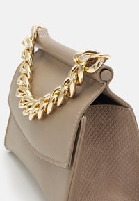 Borsa taupe con finitura opaca, pannello laterale testurizzato, patta strutturata e manico corto in chain dorato spesso su sfondo bianco.