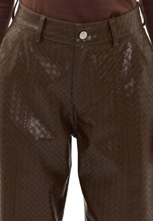 Pantalon taille haute marron foncé en matériau semblable à du cuir brillant et texturé, avec une fermeture au niveau de la taille par un bouton argenté.