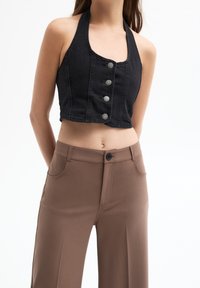 Černý denimový halter crop top s pěti kovovými knoflíky vpředu. V kombinaci s hnědými kalhotami s vysokým pasem. Hladká textury.
