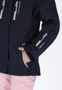 Granatowa kurtka o eleganckim fasonie i fakturowanej tkaninie. Posiada szare suwaki, kieszenie na rękawach oraz regulowane mankiety.