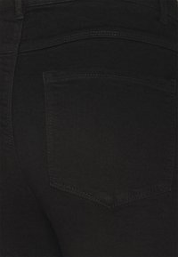 Jeans de mezclilla negra con un bolsillo trasero con costuras mínimas. La tela tiene una textura suave y un color oscuro y uniforme.