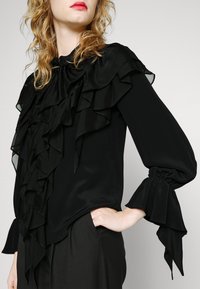 Blusa in seta nera con dettagli arricciati sulla parte anteriore e sulle maniche, con polsini arricciati e scollatura rotonda.