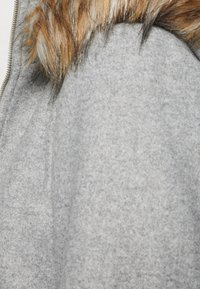 Abrigo de lana gris con una textura suave y un cuello forrado de piel, con una cremallera visible. La tela parece gruesa y cálida.