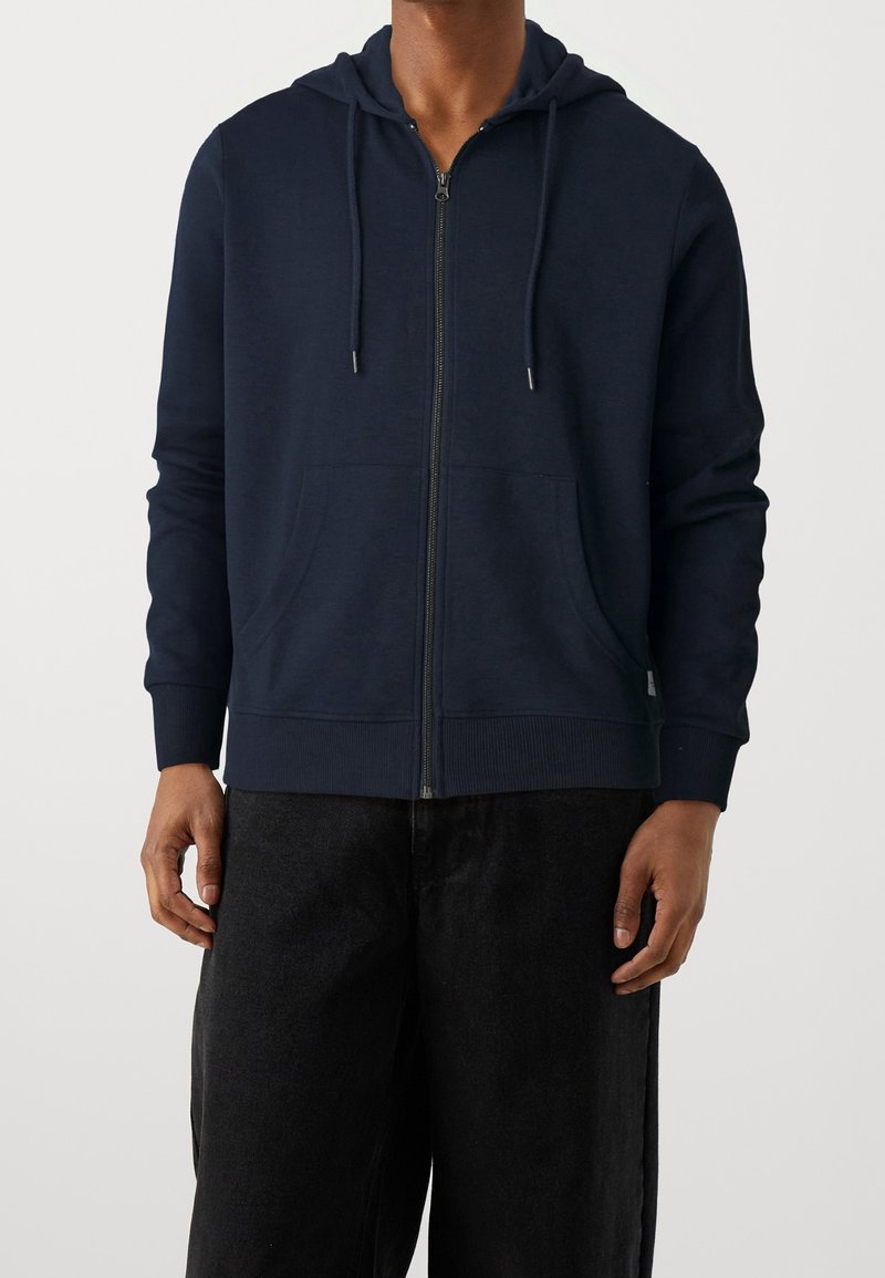 Felpa con zip di colore blu navy realizzata in tessuto morbido, con cappuccio regolabile, polsini a coste e tasca frontale a marsupio.