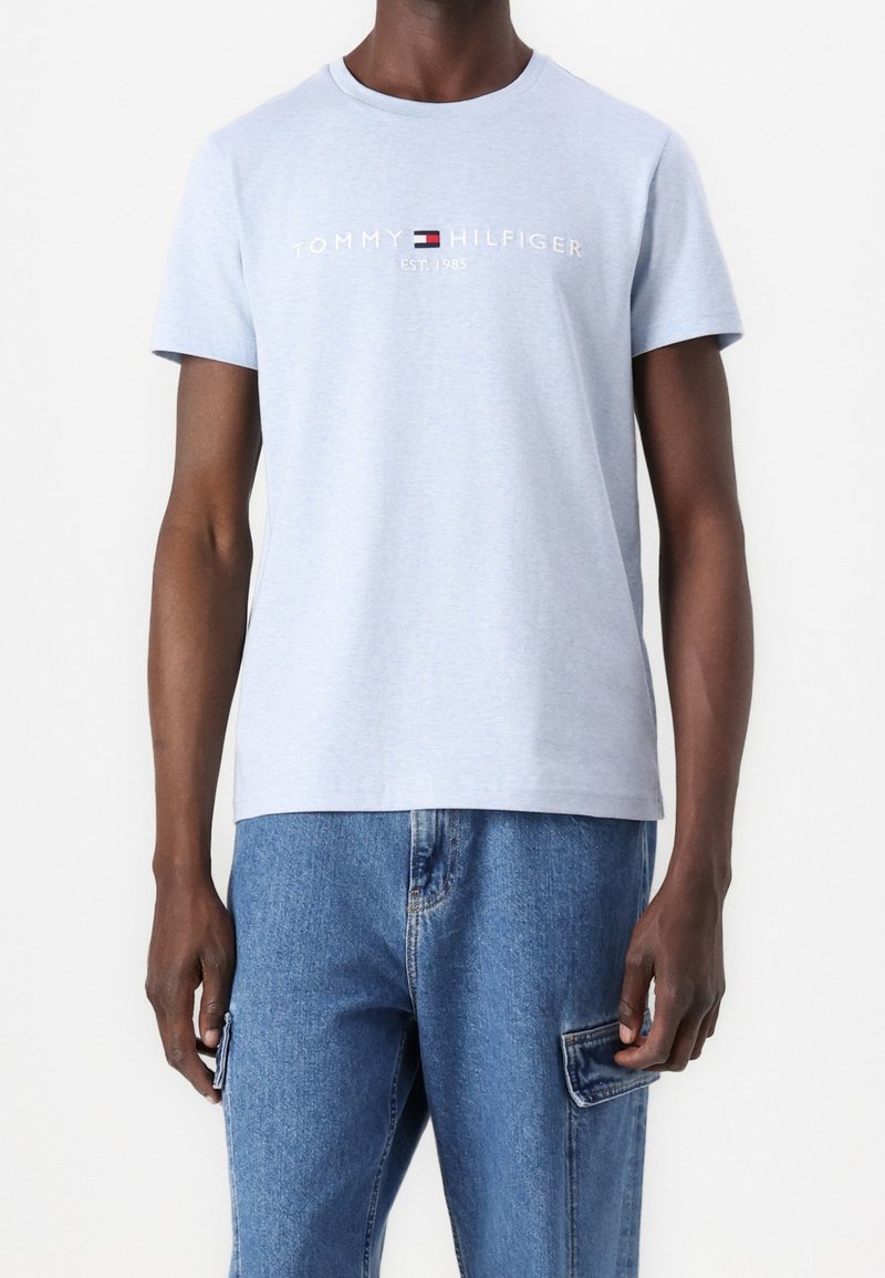 Světle modré bavlněné tričko s kulatým výstřihem a krátkými rukávy. Na přední straně je vytištěno logo "TOMMY HILFIGER EST. 1985" v kontrastních barvách.
