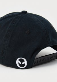 Black corduroy cap featuring a white embroidered alien logo on the side. Adjustable snapback closure at the rear. Smooth texture.