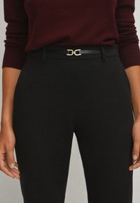 Pantalons noirs ajustés avec une texture lisse, associés à un pull bordeaux et une ceinture noire avec une boucle double-D en or.