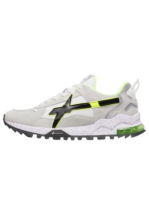 Zapatilla baja blanca y gris con logo negro y amarillo neón, suela moteada, suela exterior negra resistente y cojín de aire transparente verde en el talón.