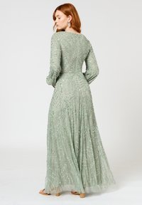 Langs mouwen, vloerlange jurk in pastelgroen. Bevat ingewikkelde kraalwerk en een soepel vallende rok met bloemenpatronen. Zachte, doorschijnende textuur.