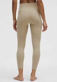Béžové legíny s vysokým pásom, so štíhlym dizajnom, bezšvíkovou textúrou a dĺžkou po členky. Obsahujú jemné švy a priliehavý strih.