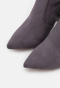 Bottes cheville en daim gris avec un bout pointu et une texture lisse, présentant des détails de couture minimalistes et un design épuré.
