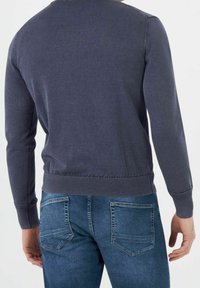 Maglione in cotone blu navy con scollatura a girocollo e orlo a costine, abbinato a jeans blu con tasche posteriori e vestibilità casual.