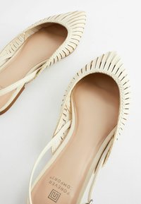 Ballerines en toile beige à bout pointu et à lanière arrière, avec des semelles matelassées étiquetées 'Forever Comfort', sur un fond blanc.