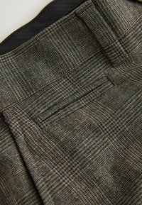 Karierte Hose in Grautönen und Brauntönen mit einer glatten Textur, versehen mit einem umgeschlagenen Bund und einem versteckten Taschendetail.