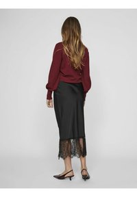 Pull bordeaux à manches bouffantes associé à une jupe midi en satin noir avec un ourlet en dentelle. Porté avec des ballerines noires à bouts pointus.