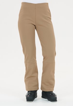 Pantaloni da sci color sabbia con una texture liscia, design a gamba ampia e cuciture visibili. Abbinati a stivali da sci neri con fibbie e profilo basso.