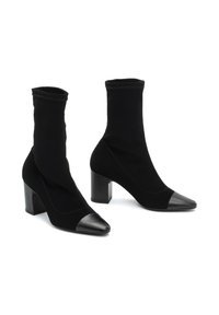 Botas negras hasta el tobillo hechas de ante con un eje elástico, punteras de cuero puntiagudas y tacones gruesos. Textura suave en toda su superficie.