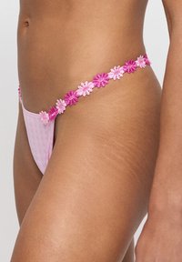 Roze slip met bloemenborduursel over de tailleband, voorzien van een textuurstof in een lichte tint, met accent op dunne banden en minimale bedekking.