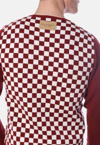 Bordeauxrot und weiße karierte Strickjacke mit einem rechteckigen braunen Etikett auf der Rückseite, mit glatter Oberfläche und gerippten Bündchen.