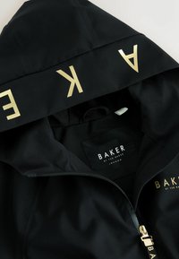 Čierna bunda s kapucňou so zlatým nápisom "BAKER" na kapucni a zipsom, vnútorná etiketa s nápisom "Baker by Ted Baker London."
