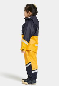 Gul och marinblå vattentät regndräkt med reflexstripes; har huva, elastiska ärmslut och matchande stövlar, designad för barn.
