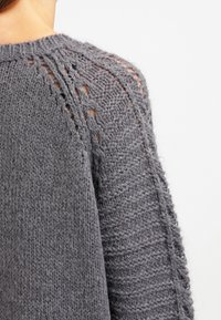 Gray knitted sweater featuring textured patterns and open stitch details on the shoulder; soft material with a loose fit.