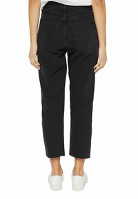 Pantalones de mezclilla negros con corte recto, que presentan un dobladillo deshilachado, dos bolsillos traseros y combinados con zapatillas blancas.