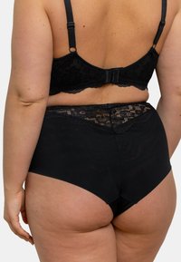 Ensemble de lingerie noire comprenant un soutien-gorge avec un dos en dentelle et des culottes taille haute, mettant en valeur des détails en dentelle élaborés et une texture de tissu lisse.