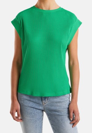 Mouwloos geribd groen topje gedragen door een persoon met lichtblauwe jeans, getoond van nek tot heupen tegen een witte achtergrond.