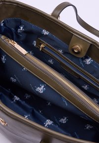 Borsa a tracolla in pelle verde oliva con accessori dorati; l'interno presenta una fodera in tessuto blu navy con un motivo azzurro ripetuto e scomparti con zip.