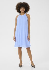 Light blue pleated dress with halter neck design, airy texture, and a scalloped hem, paired with black and white striped heels.