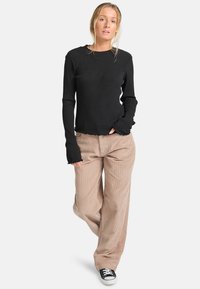 Schwarzes geripptes Langarmoberteil mit ausgefranstem Saum, kombiniert mit beigen Cordhosen im weit geschnittenen Stil und schwarzen Schnürsneakern. Minimalistisches Design.