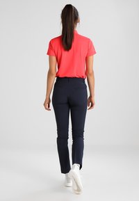 Rosa kortärmad polo skjorta i kombination med marinblå slim-fit byxor och vita sneakers. Outfiten har en slät textur och en figurnära design.