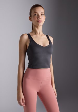 Un débardeur noir court avec des bretelles larges et un décolleté en V, associé à un legging taille haute rose en matière lisse et extensible.