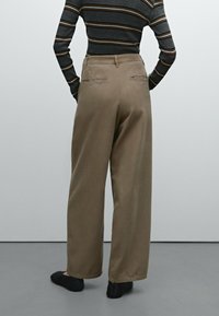 Brązowe spodnie typu wide-leg z tylnymi kieszeniami, wykonane z miękkiego materiału. Na wysokości talii noszona jest dopasowana bluzka w paski.