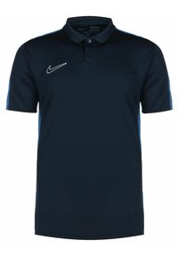 Polo bleu marine avec un col noir, manches courtes et accents latéraux bleu clair. Présente un logo Nike blanc sur la poitrine. Texture de tissu lisse.
