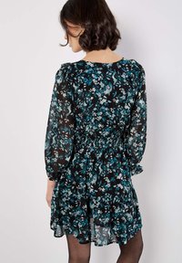 Robe noire à fleurs avec une taille smockée, de longues manches bouffantes et une jupe en couches. Présente des motifs floraux teal et blancs.