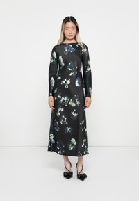 Long black floral dress with green and blue abstract patterns. Smooth texture, long sleeves, round neckline, paired with black bow sandals.