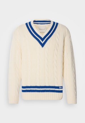 Suéter crema de punto trenzado con un profundo escote en V, que cuenta con un cuello y dobladillo a rayas en azul y blanco. Muestra "Gant" en azul en el borde inferior.
